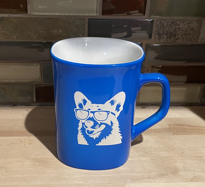 Blue ceramic round coffee mug with a corgi wearing sunglasses engraved on the front. Corgi Mug