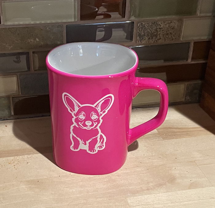 Pink ceramic round coffee mug with a sitting corgi engraved on the front. Corgi Mug