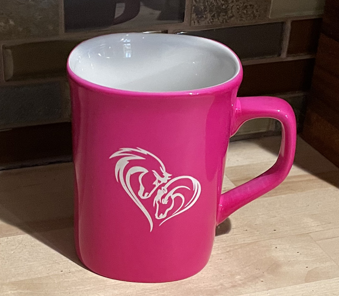 Pink ceramic round coffee mug with a 2 horse heads making a heart engraved on the front. Equestrian Mug