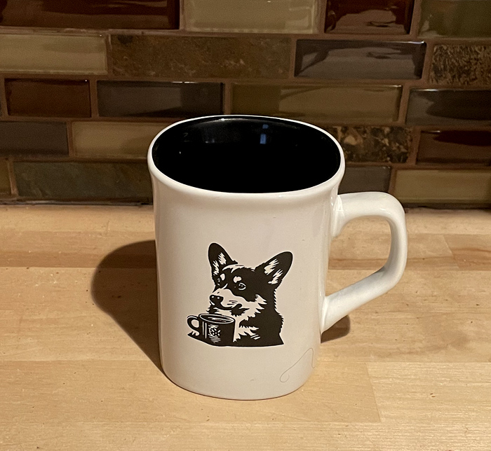 White ceramic round coffee mug with a corgi drinking coffee engraved on the front. Corgi Mug
